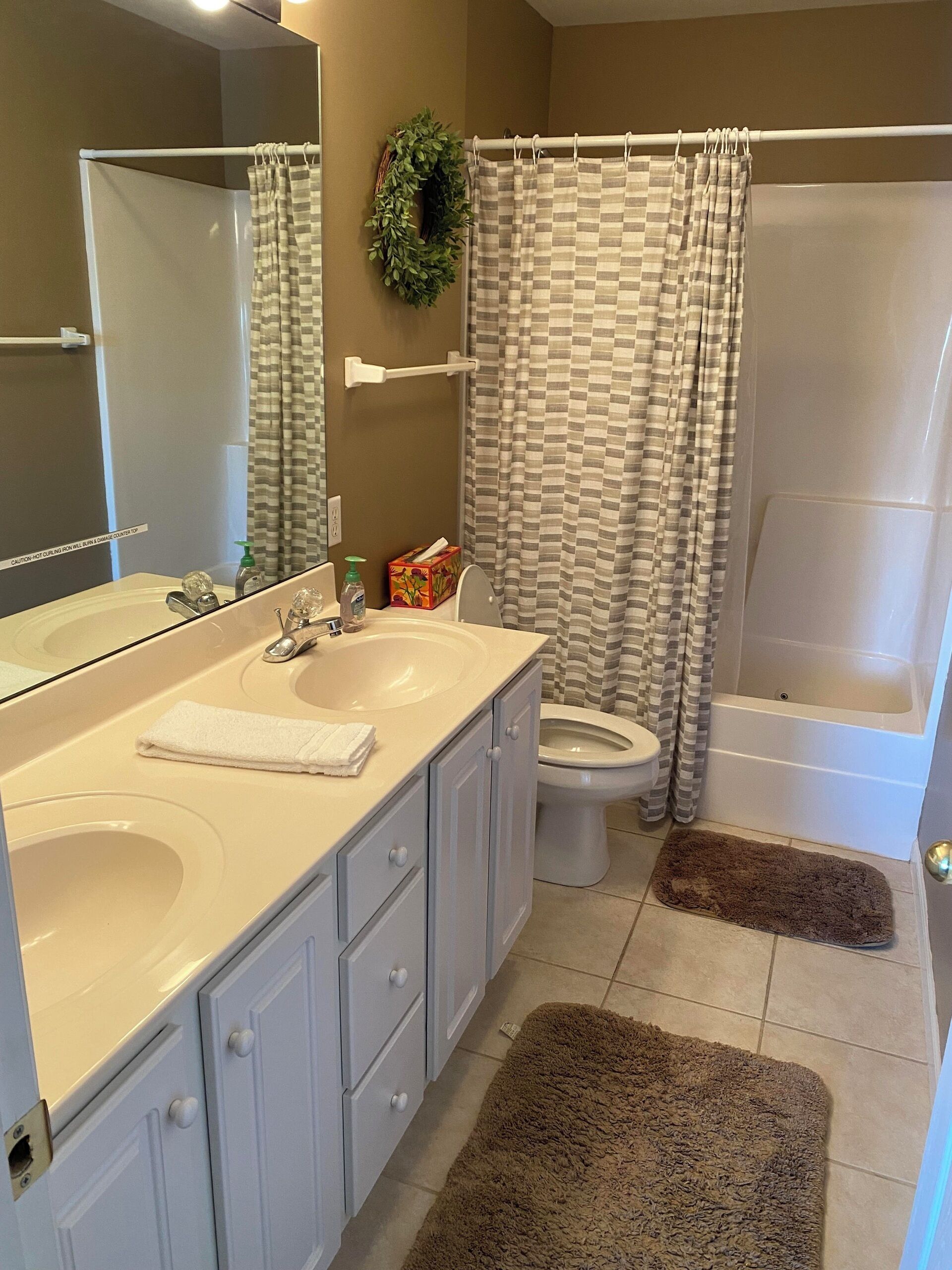 A bathroom with a double sink, toilet, bathtub, and a shower curtain.
