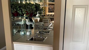 Une cuisine avec un pare-feu en verre, des meubles blancs, un évier et un coin repas avec des chaises.