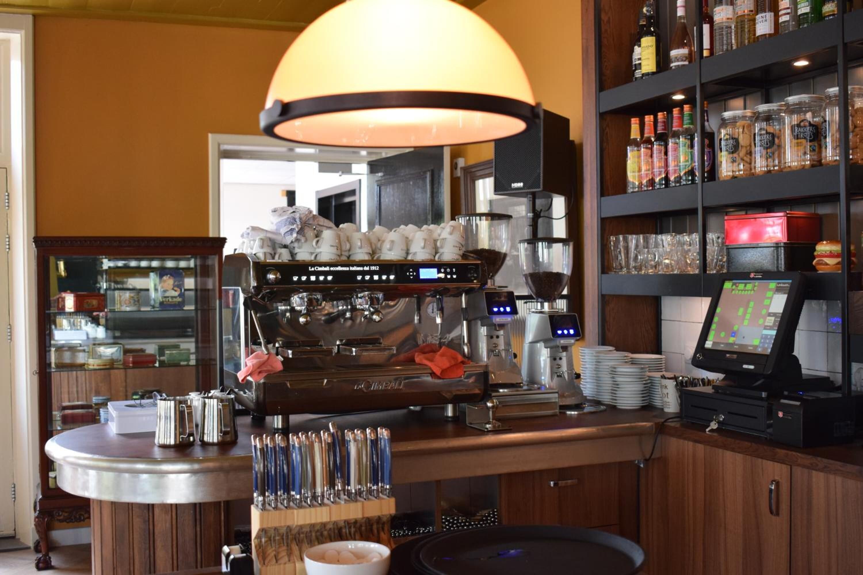 A bar area with a coffee machine, a cash register, and shelves stocked with snacks and bottles.