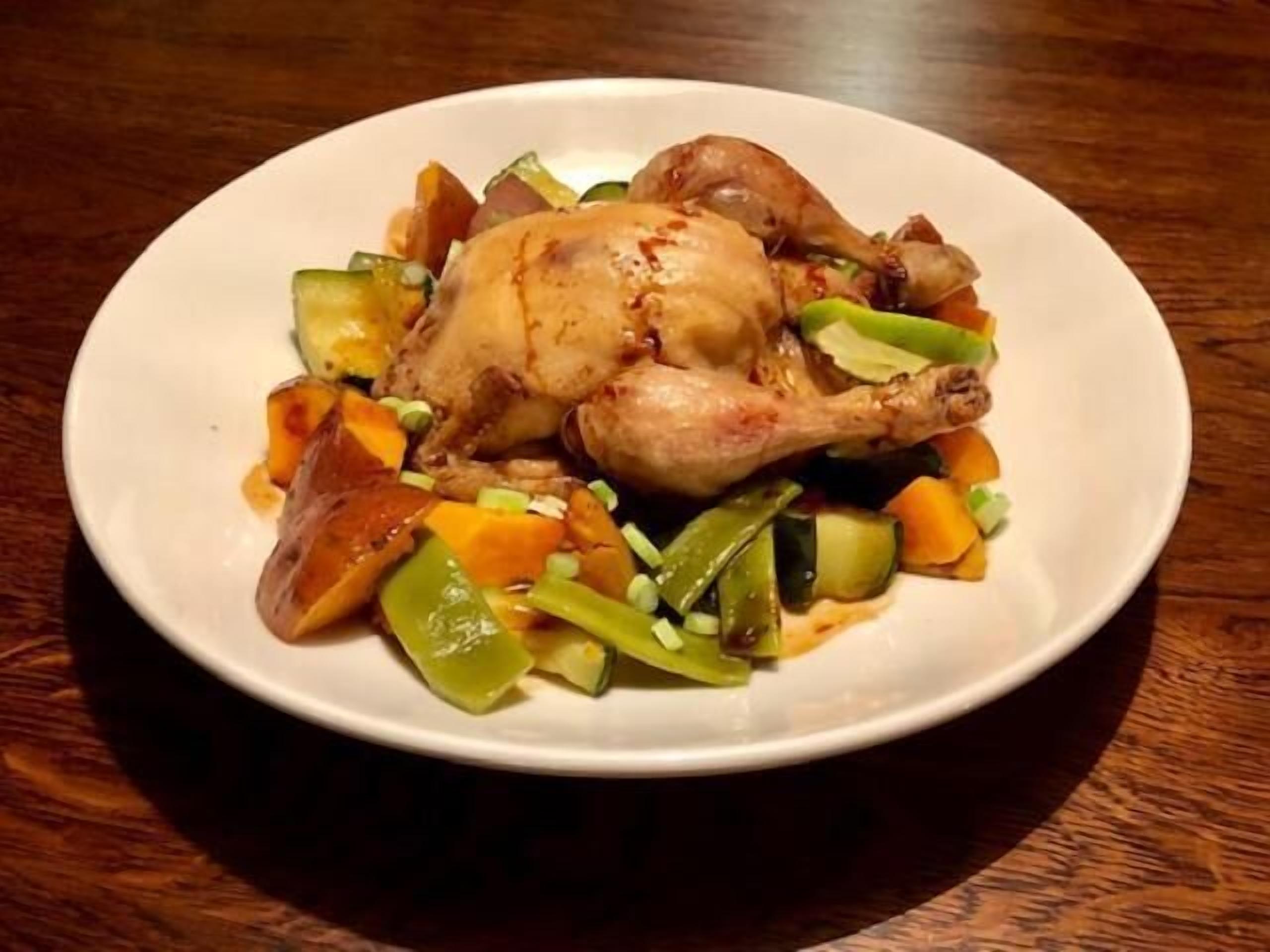 A plate of roasted chicken with vegetables on a wooden table.