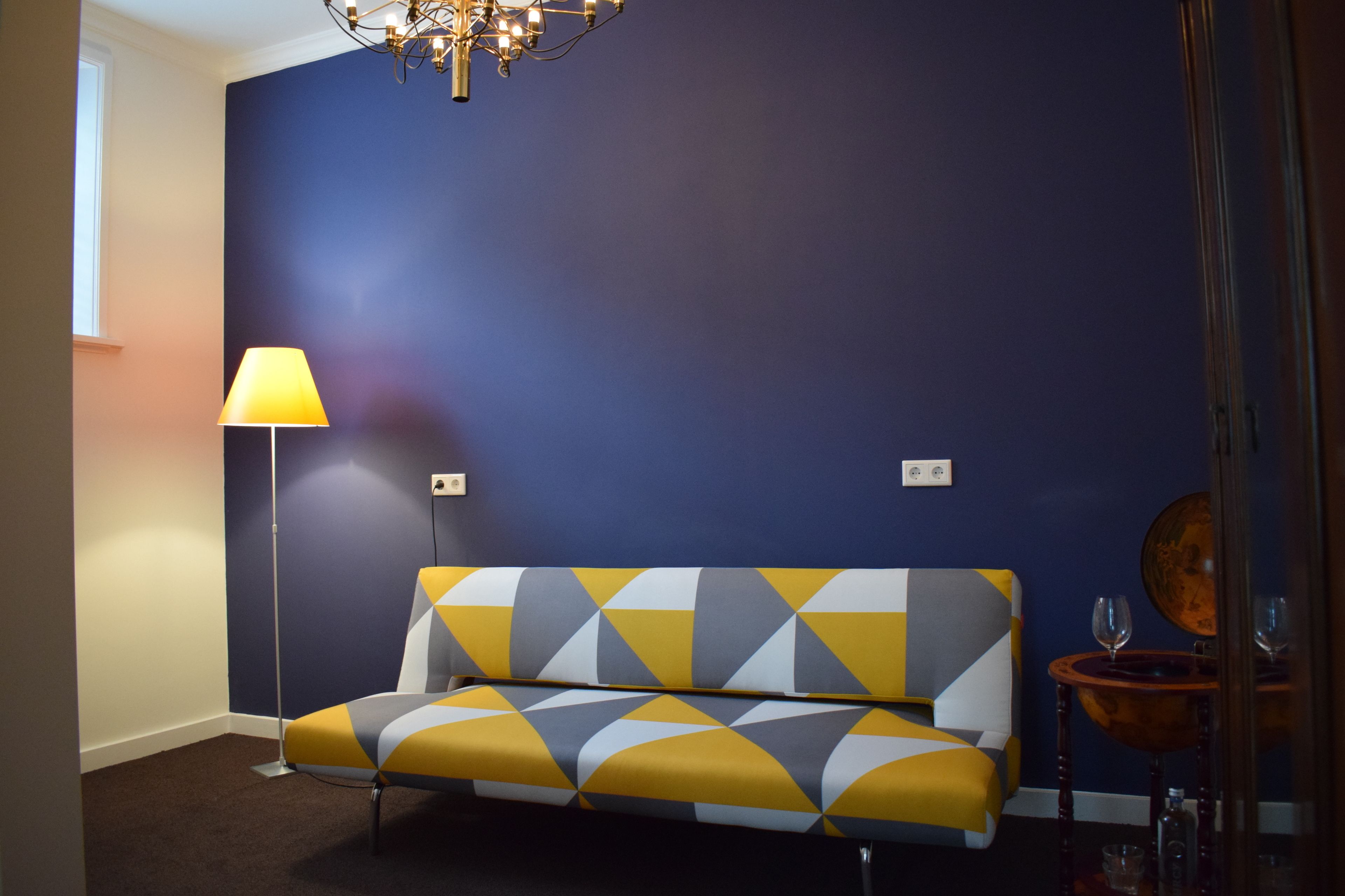 A room with a sofa against a dark blue wall, a floor lamp, and a small table with glasses.