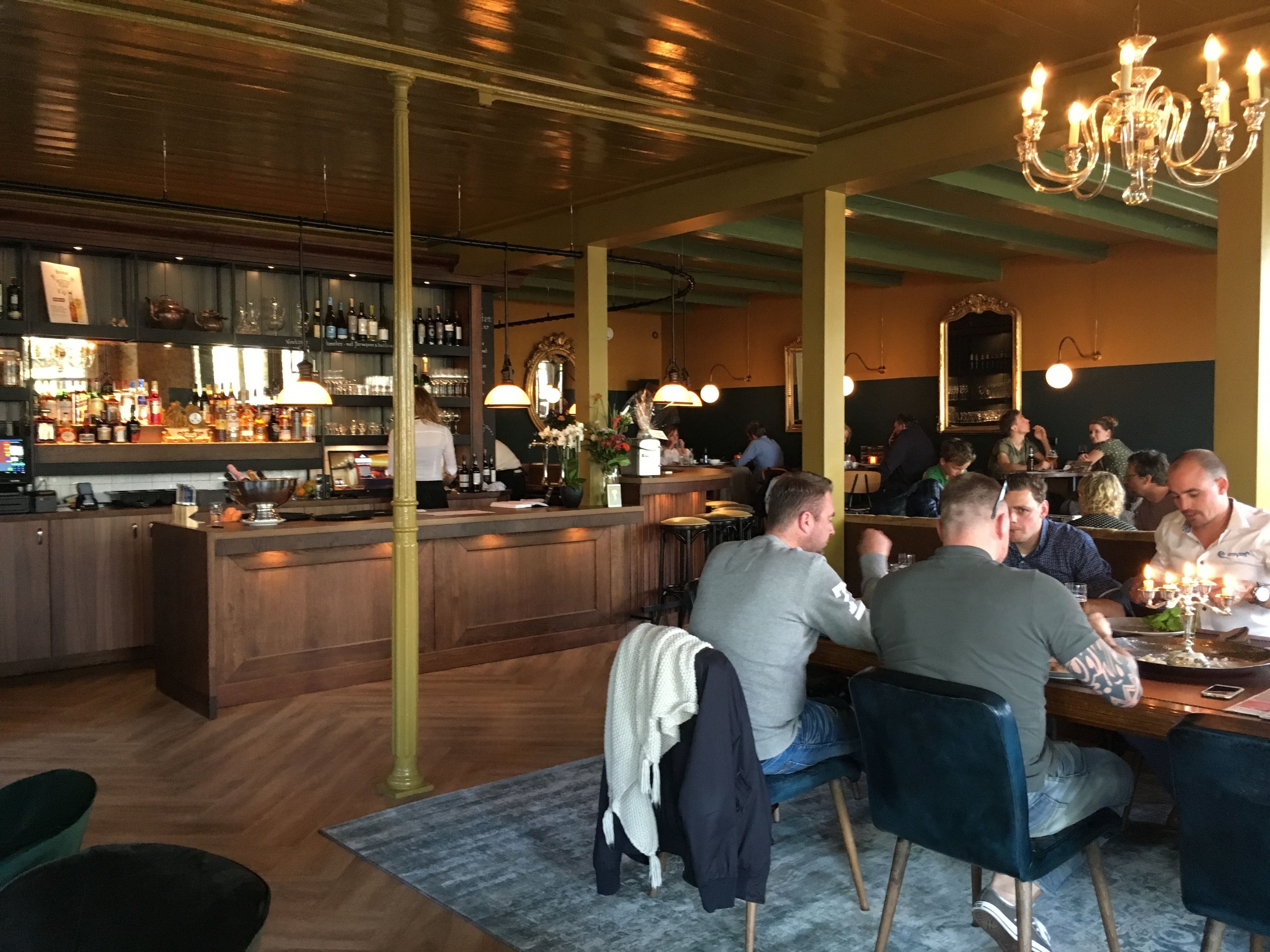 Een restaurant met een bar, houten vloeren en een kroonluchter.