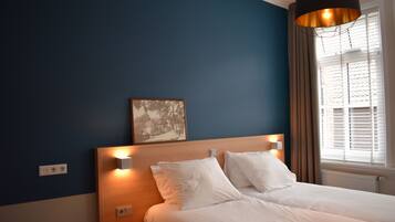 A bedroom with a bed, bedside lamps, a wall-mounted artwork, and a window with curtains.