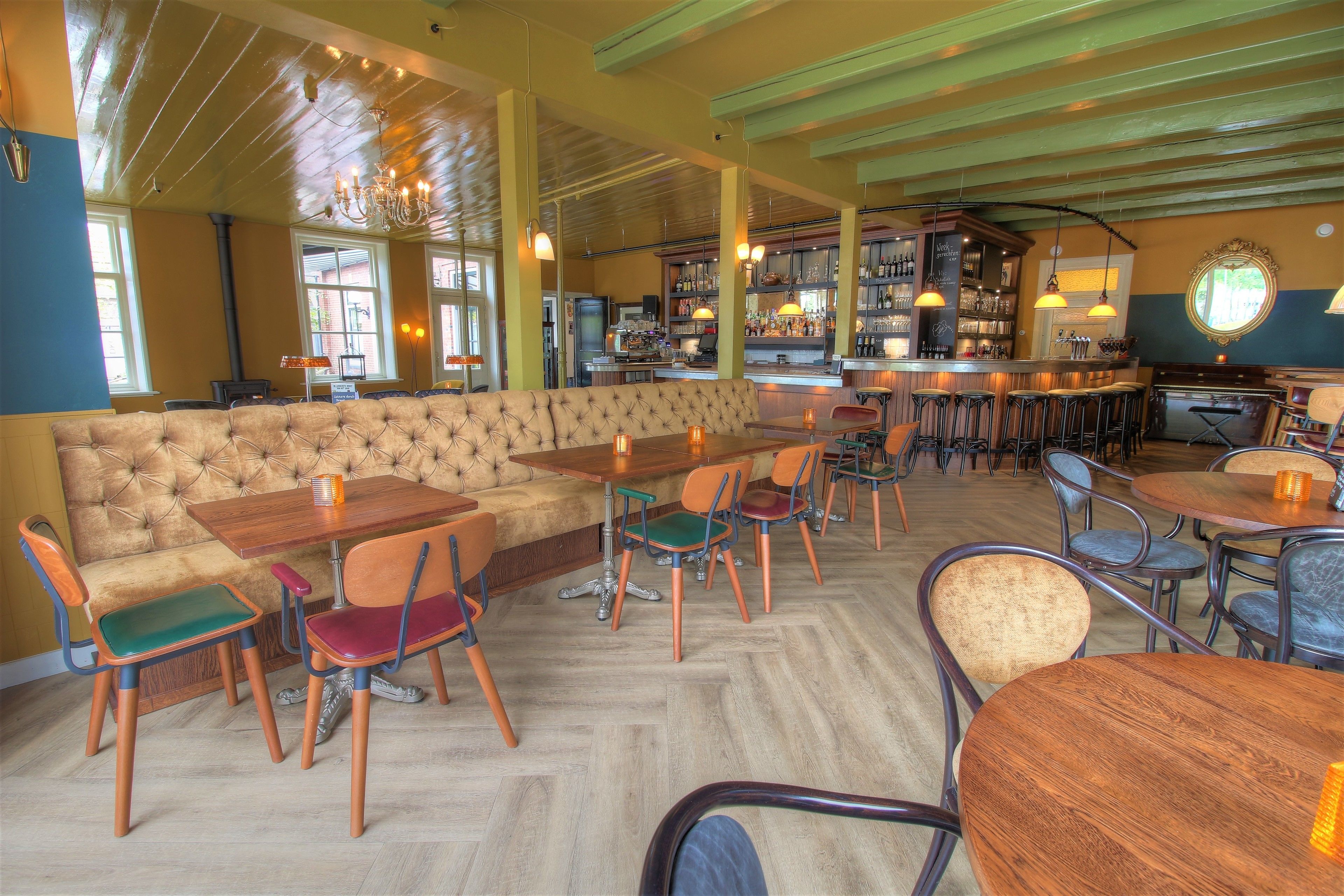 Zona de bar con mesas y sillas de madera, barra y un área de estar con un banco acolchado.