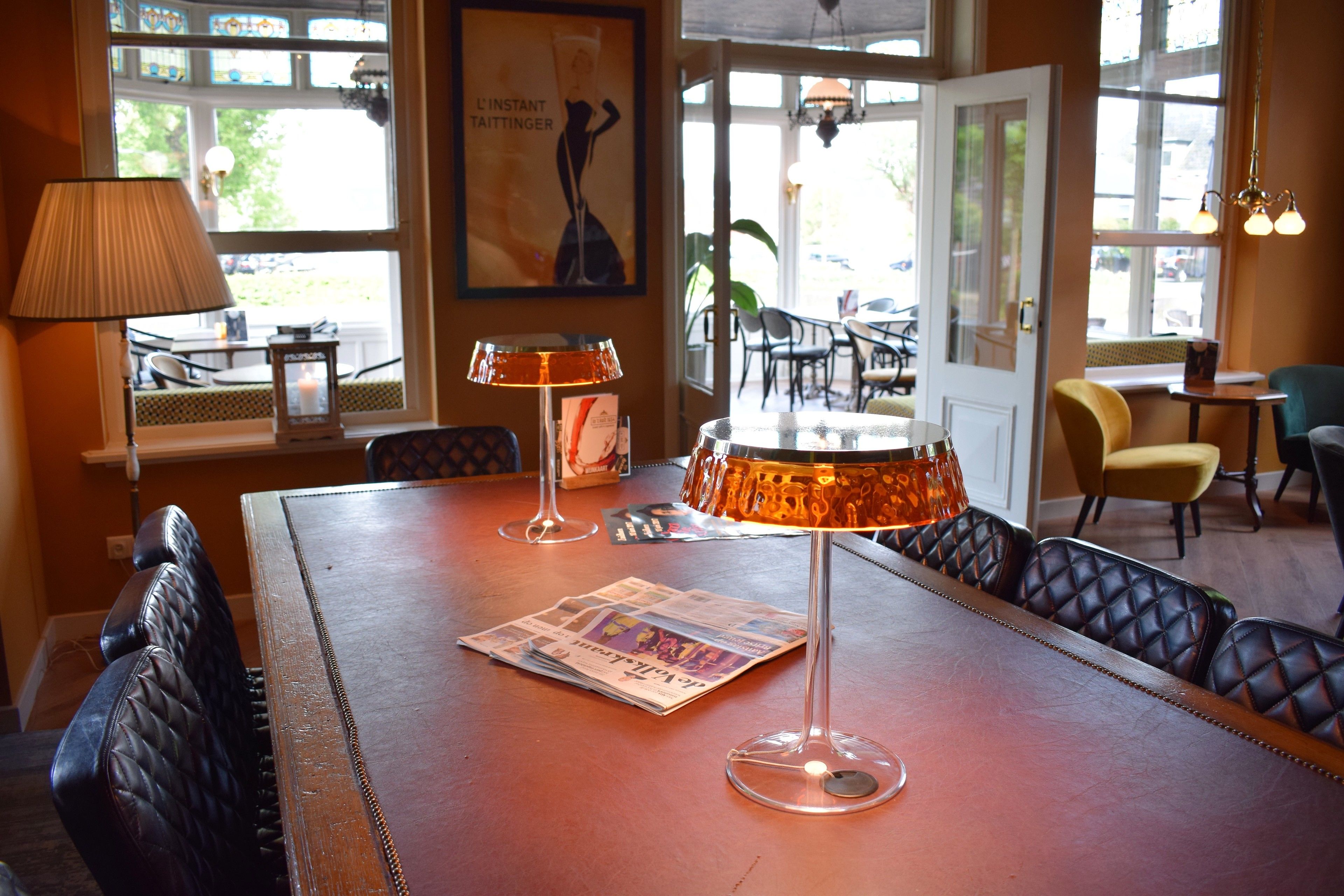 A dining area with leather seating, a table with newspapers, a lamp, and a poster on the wall.
