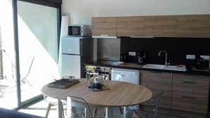 A modern kitchen with a built-in microwave, coffee maker, and dishwasher. There is a round dining table with chairs and a window providing natural light. - Superb entirely new housing (Leychert)