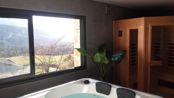 Une salle de bain avec une baignoire, une fenêtre donnant sur un paysage et une porte en bois.