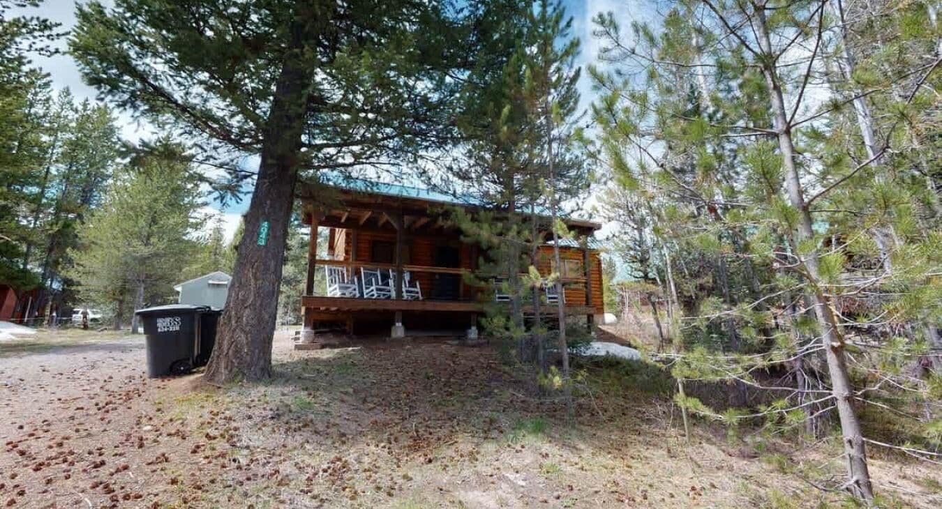 Une cabane dotée d’un porche, entourée d’arbres et offrant une vue sur un ciel dégagé.