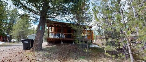 Une cabane dotée d’un porche, entourée d’arbres et offrant une vue sur un ciel dégagé.