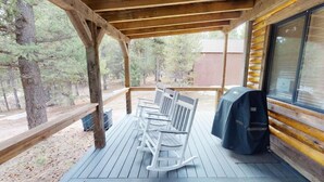 Un espace extérieur abrité doté d’une terrasse en bois, de fauteuils à bascule blancs et d’un barbecue.
