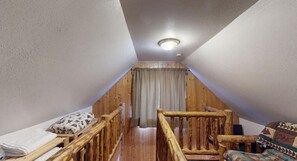 Une petite pièce mansardée, chaleureuse et accueillante, avec un plafond en pente, des meubles en bois et une seule fenêtre agrémentée de rideaux.