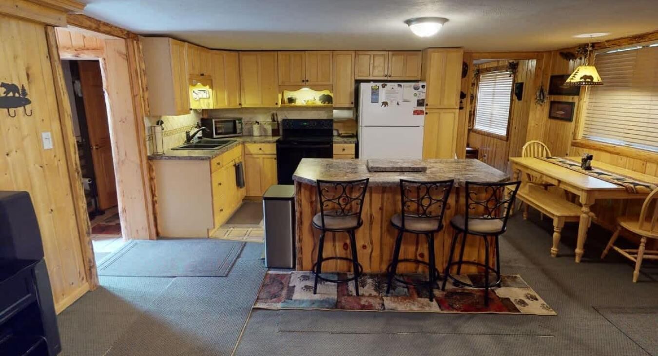 Eine kompakte Küche mit Holzausstattung, einem Kühlschrank, einer Mikrowelle und einem Herd. An der Theke stehen drei Barhocker.