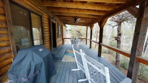 A wooden deck with a covered seating area, a grill, and a view of the surrounding forest. - Yellowstone NP | Sleeps 8 | Fire Pit & BBQ (Island Park)
