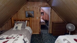 A cozy attic bedroom with a sloped ceiling, a bed with a polar bear-themed duvet, a wooden headboard, and a small fan. - Yellowstone NP | Sleeps 8 | Fire Pit & BBQ (Island Park)