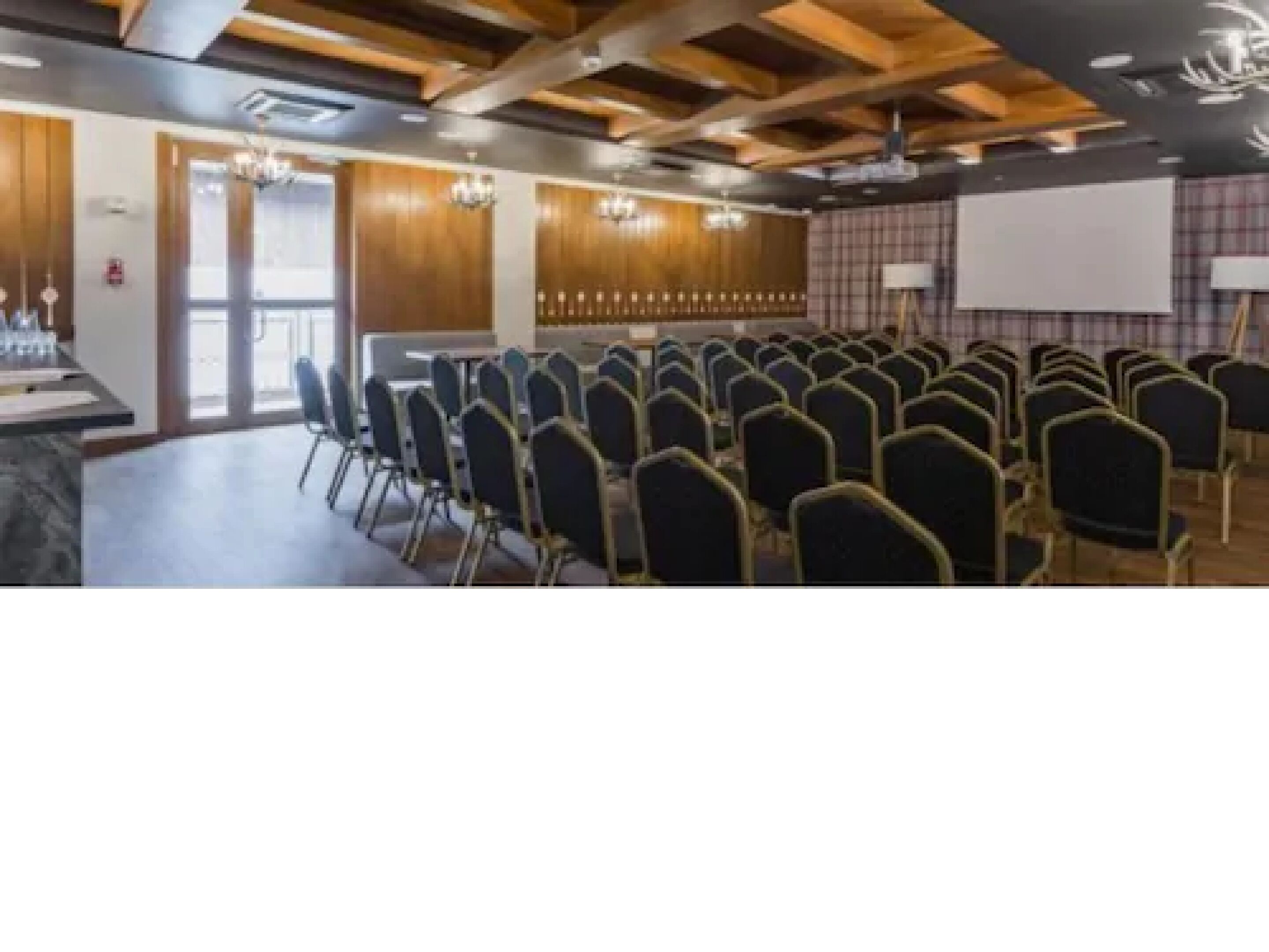 A conference room with rows of chairs, a projector screen, and a wooden ceiling.
