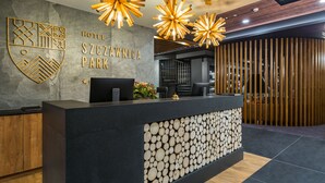 A hotel reception desk with a modern design, featuring a logo on the wall, a computer, and a decorative wall with logs. - Hotel Szczawnica Park Resort & Spa (Szczawnica)