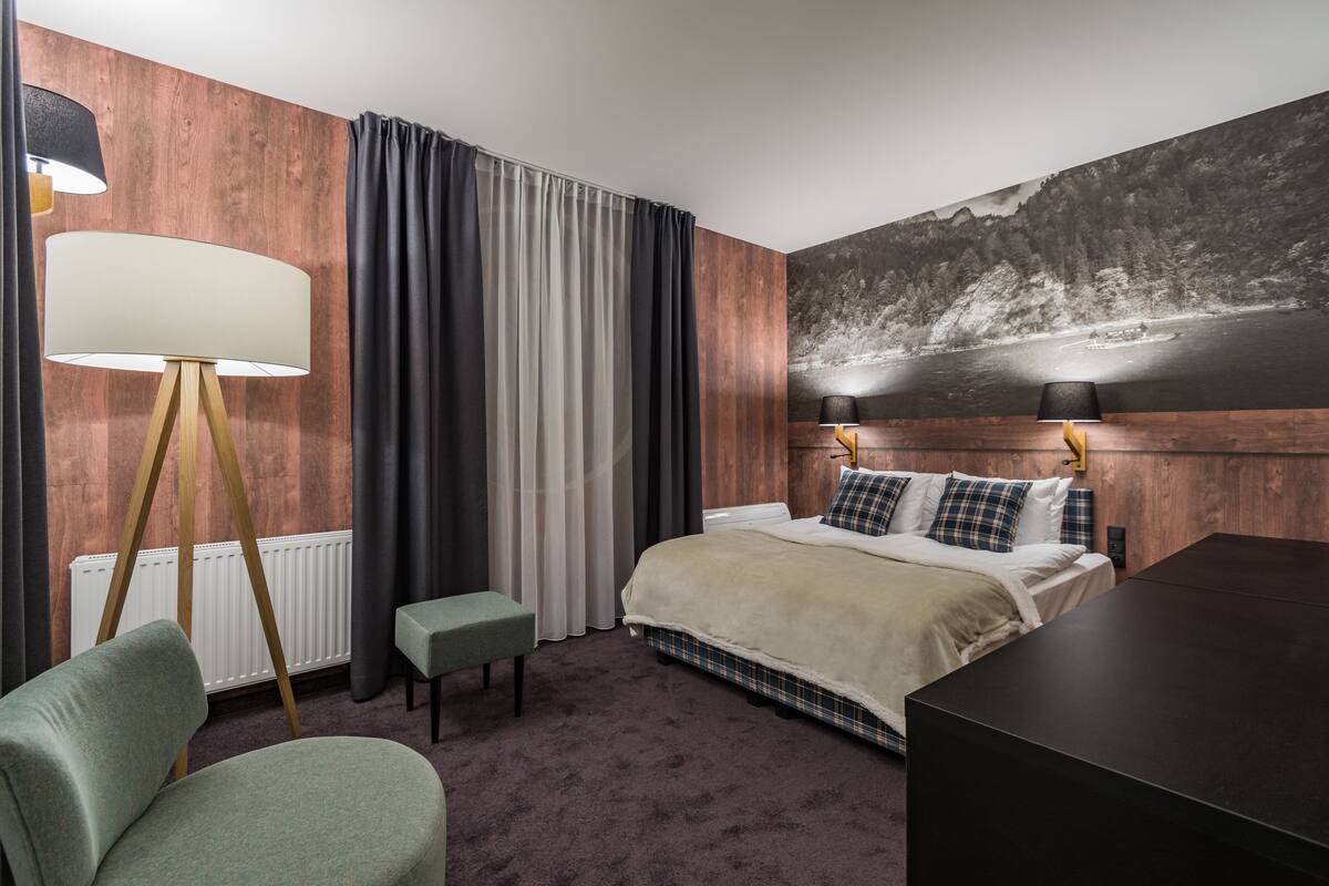 A hotel room with a large bed, a desk, a chair, a lamp, and a painting on the wall.
