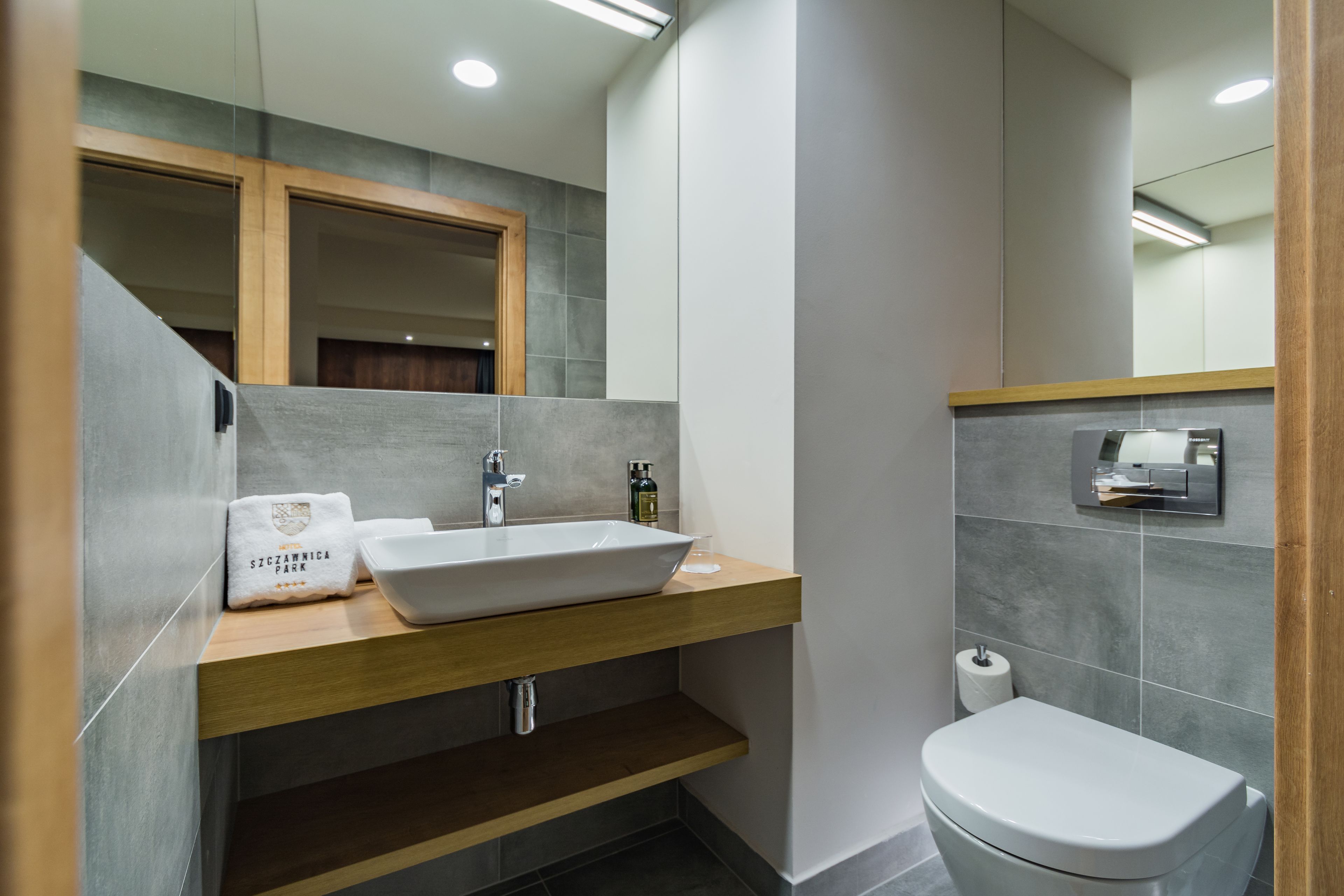 A modern bathroom with a wooden vanity, a large mirror, a white sink, and a toilet.