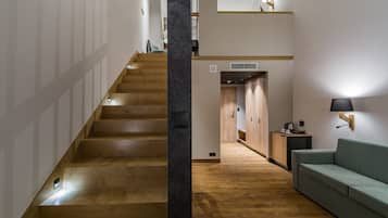 A staircase leading to a second floor, a wooden floor, a green sofa, and a wall-mounted lamp.
