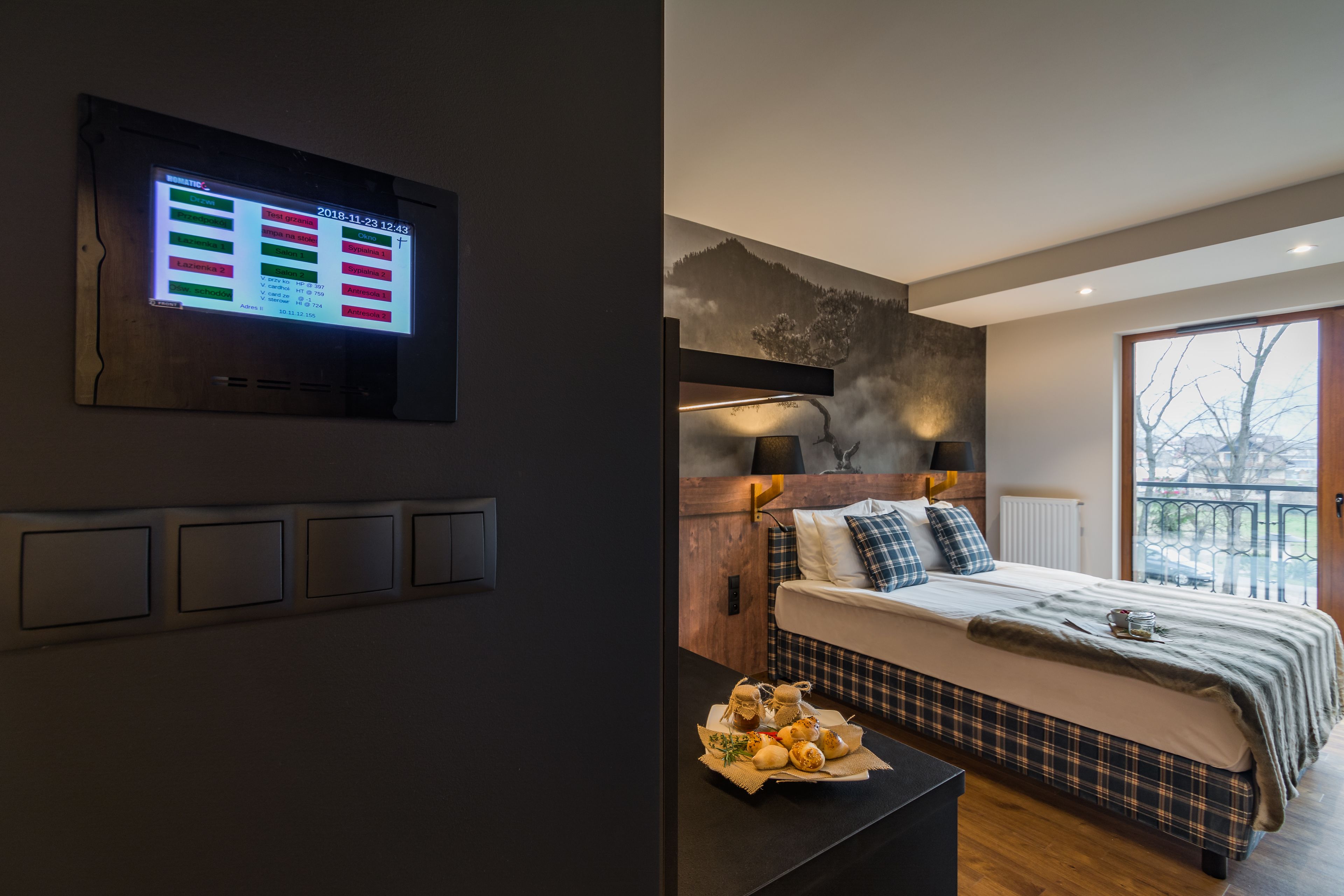Un dormitorio moderno con cama, televisor montado en la pared y vistas al exterior a través de un amplio ventanal.