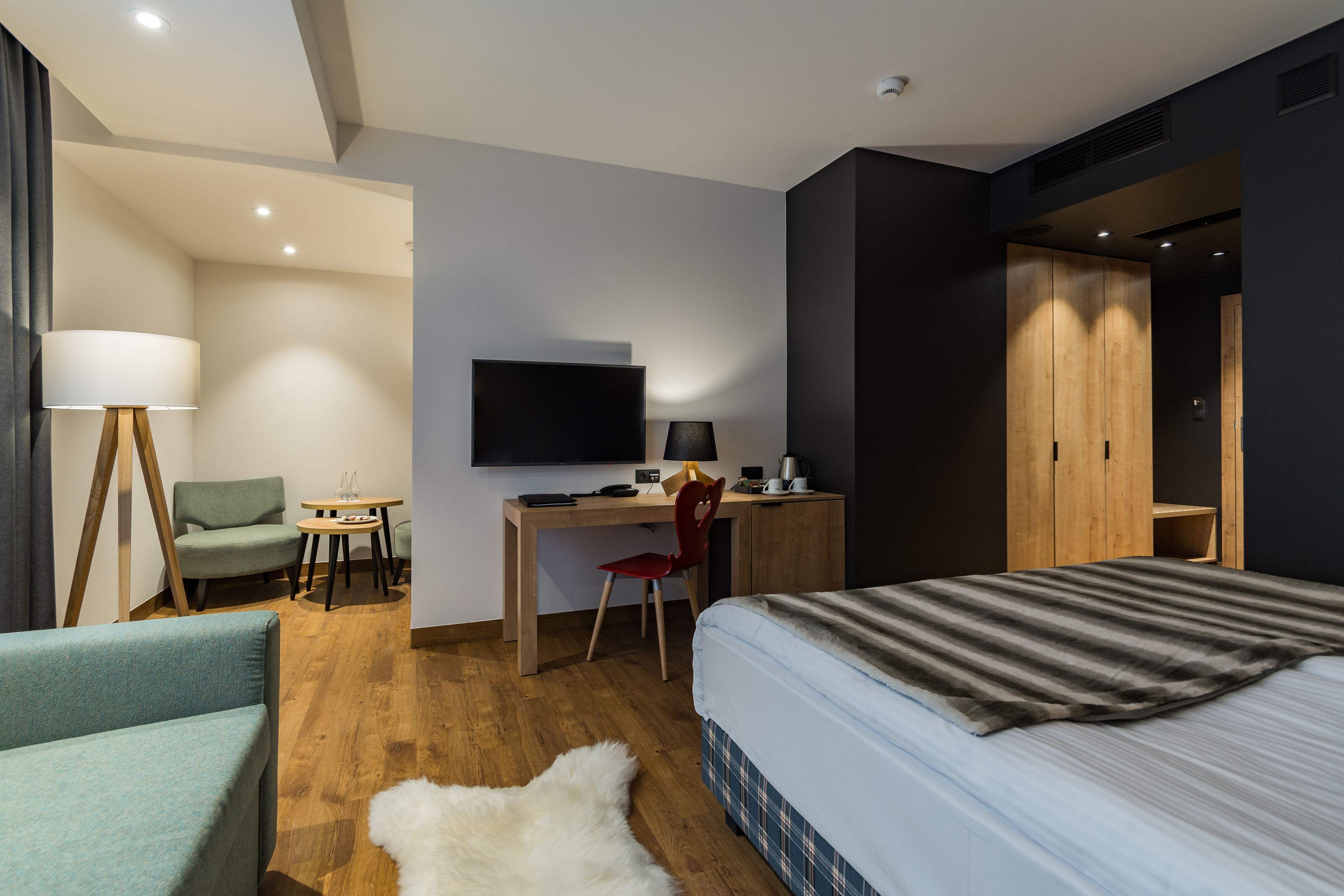 A modern hotel room with a bed, a desk, a TV, a chair, and a sofa.