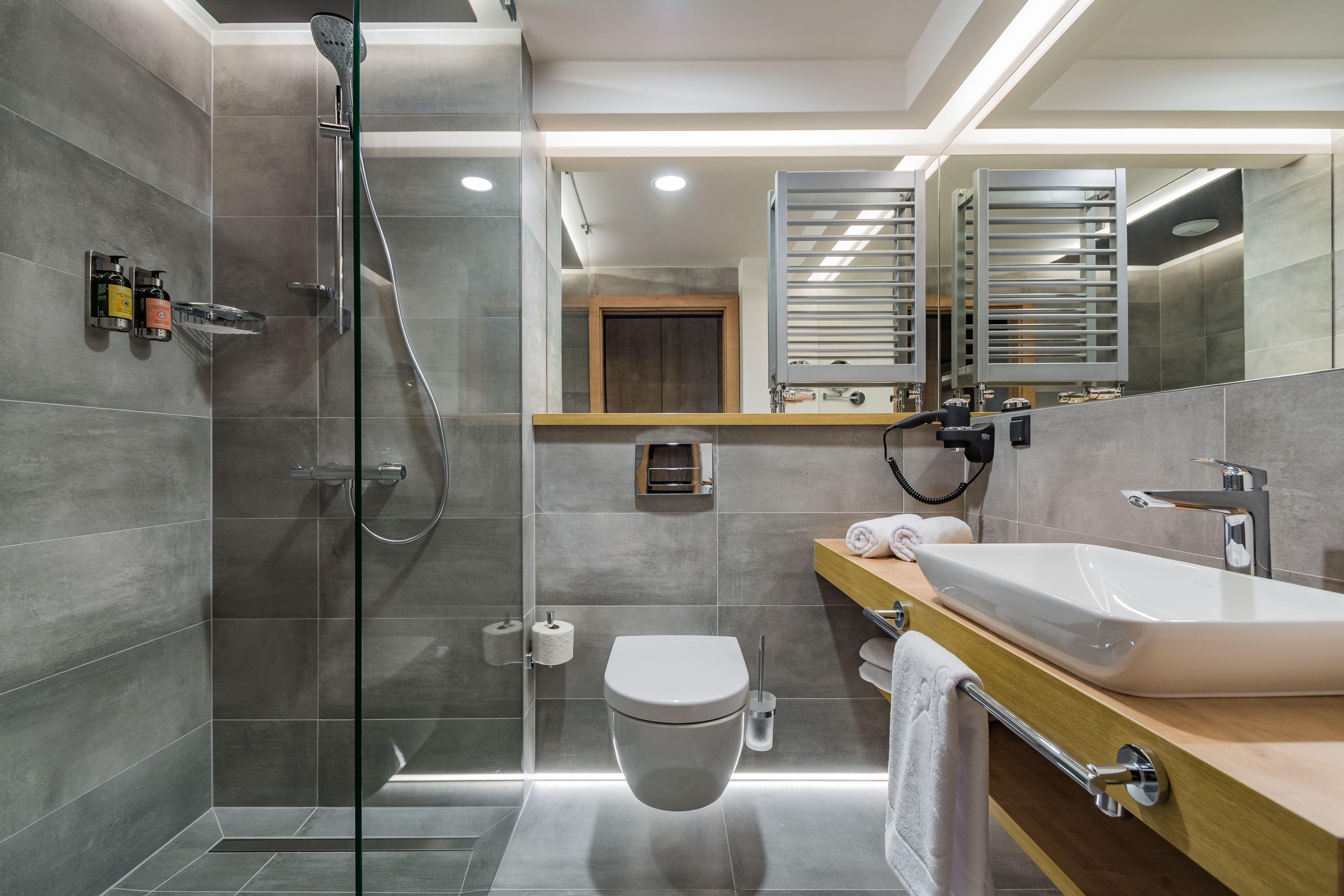 A modern bathroom with a glass-enclosed shower, a white toilet, a large sink, and a wooden vanity.