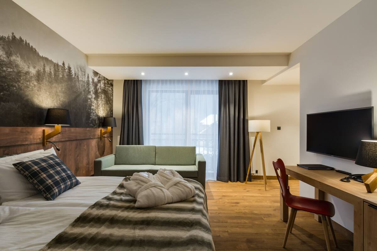 A hotel room with a bed, a desk, a chair, a television, and a large window with curtains.
