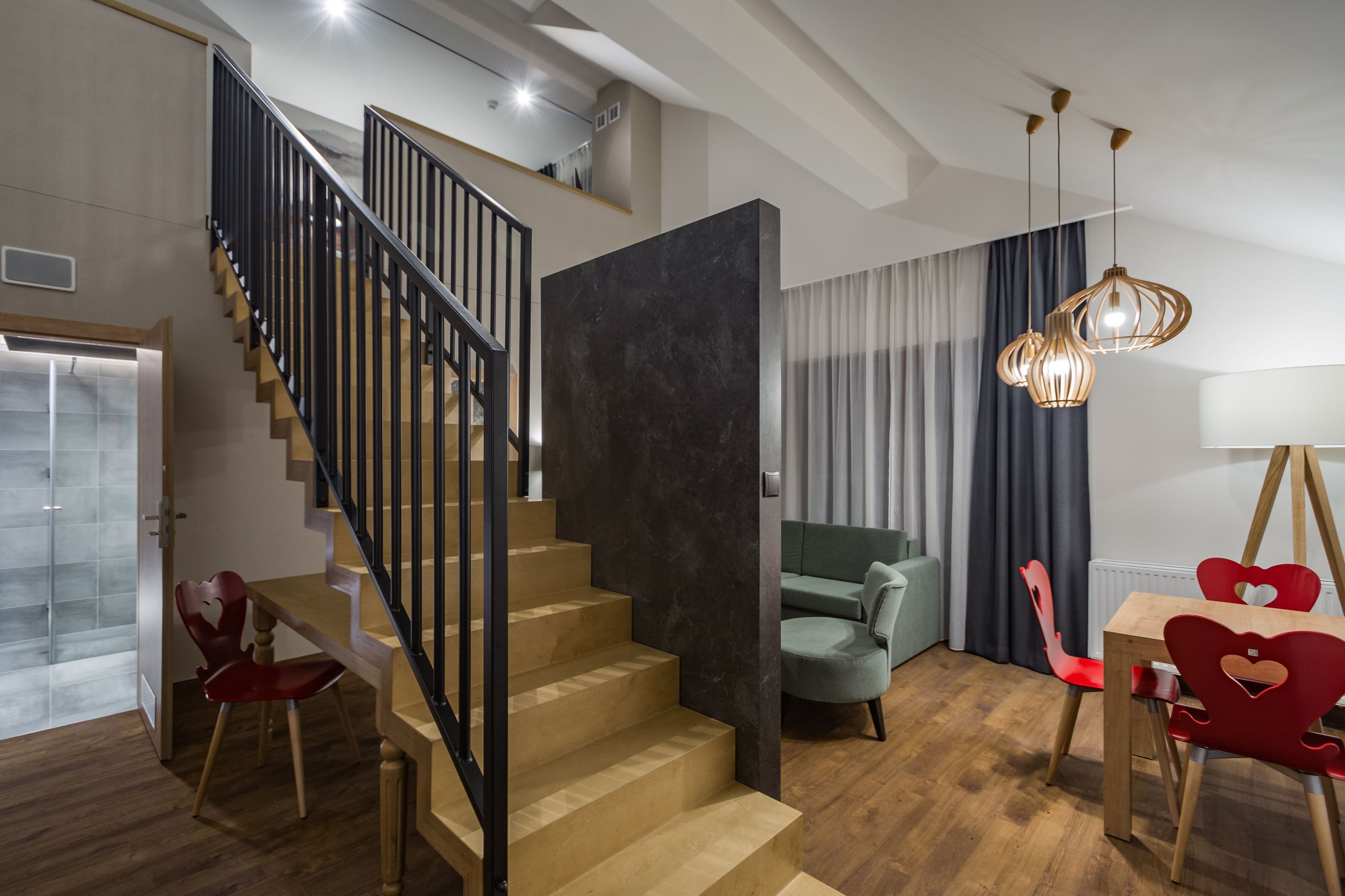 Un espace de vie moderne comprenant un escalier, un coin repas avec des chaises en forme de cœur et un coin salon confortable avec un canapé vert.