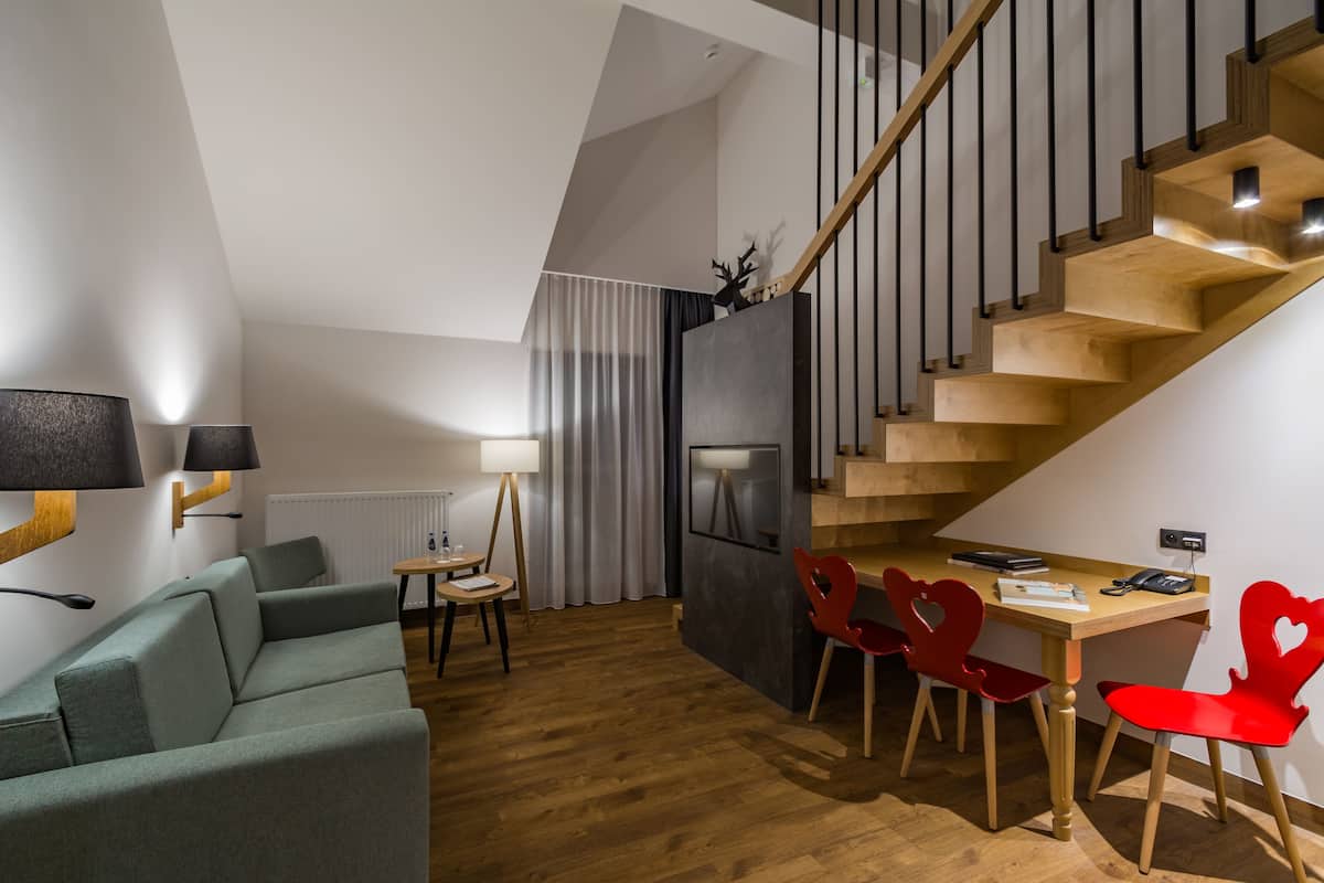A modern living space with a wooden staircase, a dining area with red chairs, a green sofa, and a small table with a lamp.