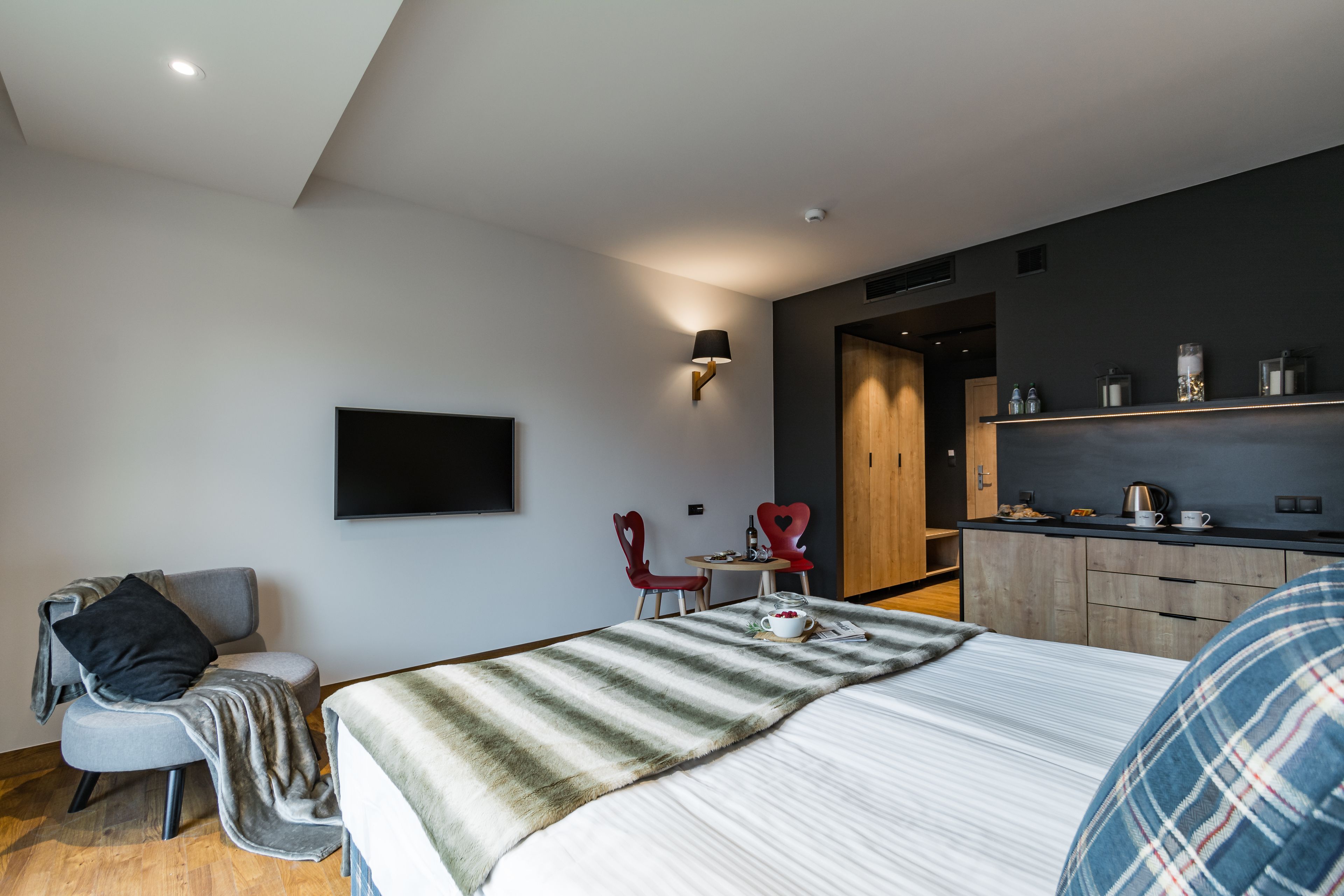 A modern hotel room with a large bed, a desk with a chair, a flat-screen TV, and a kitchenette.