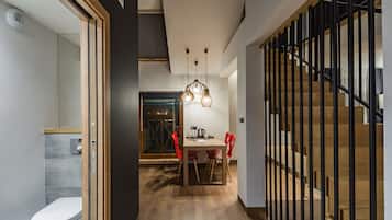 Un interior moderno con una escalera de madera, una zona de comedor con sillas rojas y una cocina a la vista a través de un umbral abierto.