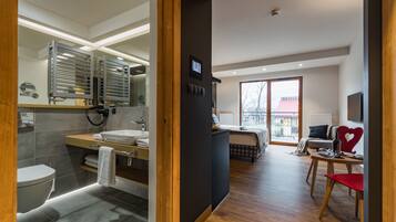 A modern hotel room with a bathroom, a living area with a sofa and a dining table, and a balcony with a view.