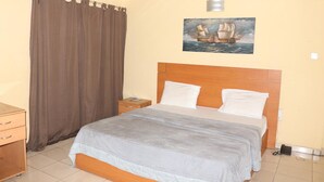 Ein Schlafzimmer mit Bett, Nachttisch, Holz-Kopfteil, einem Wandbild eines Schiffes und einem Vorhang.