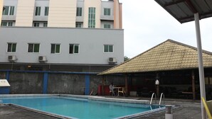 Ein Schwimmbad mit überdachtem Bereich und einem Gebäude im Hintergrund, das mehrere Fenster sowie Klimaanlagen aufweist.