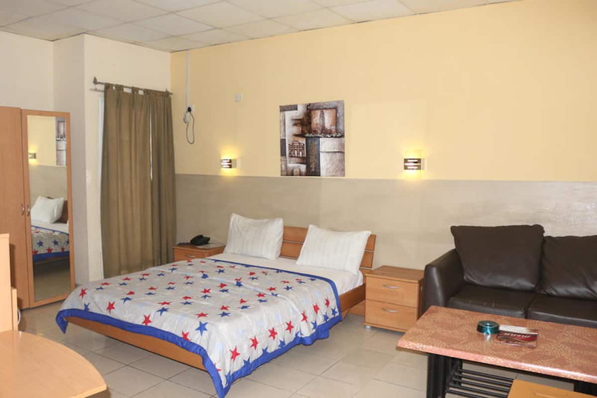A hotel room with a bed, a desk, a chair, a sofa, a mirror, and a wall-mounted artwork.