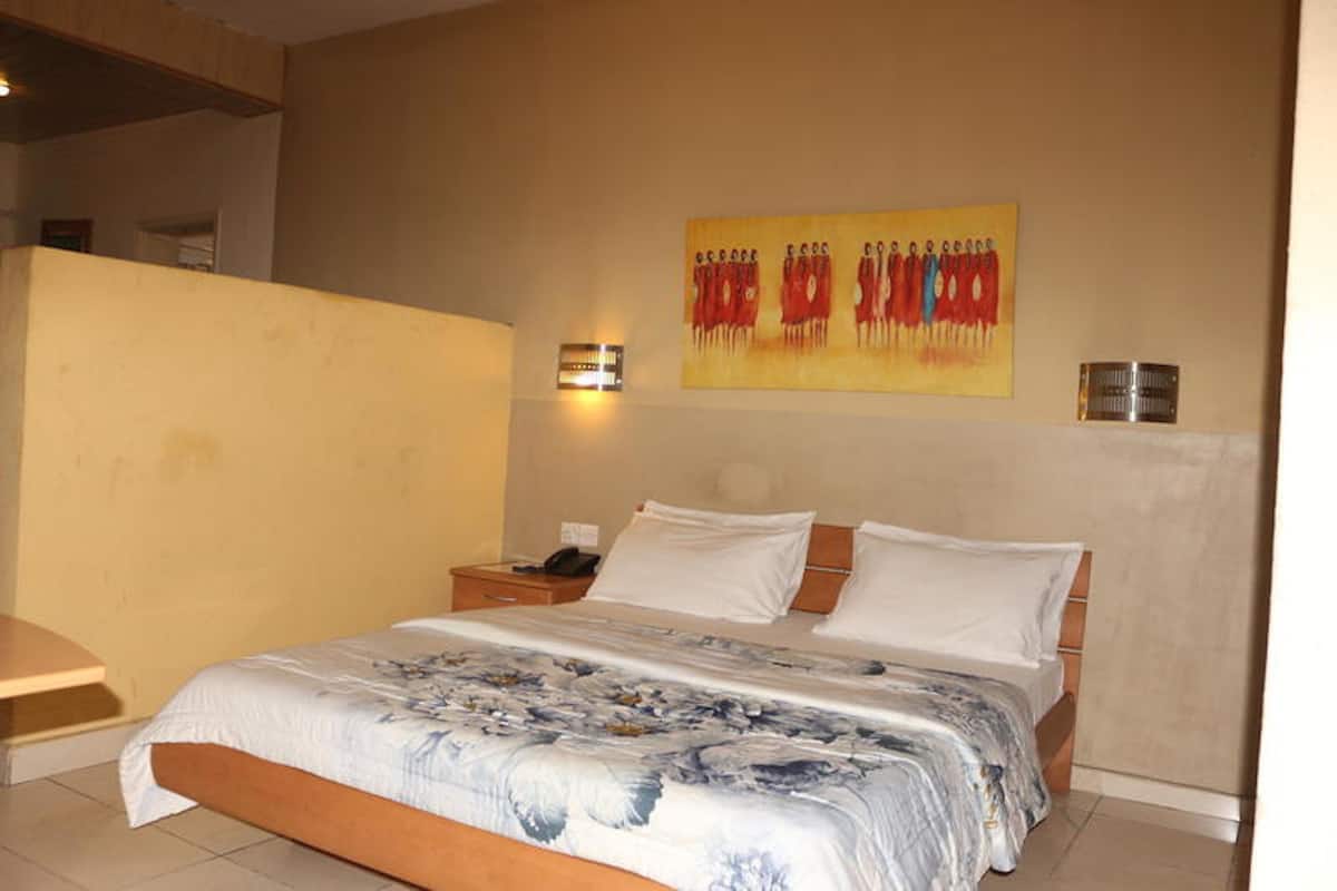 A bedroom with a bed, nightstand, wall-mounted lamp, and a painting.