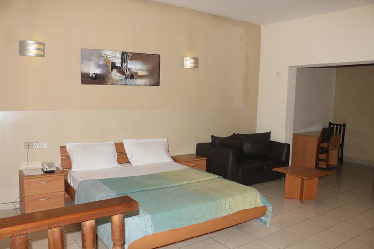 A hotel room with a bed, a black leather sofa, a wooden coffee table, and a wooden bench.
