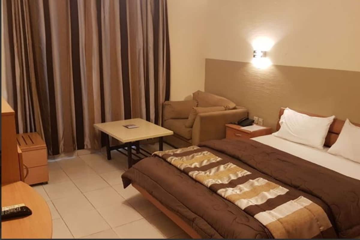 A hotel room with a bed, a sofa, a small table, a nightstand, and a lamp.