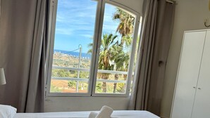 A hotel room with a bed, a window with curtains, and a view of palm trees and buildings. - Bellavista - Villa with panoramic sea views and large terraces (Calpe / Calp)