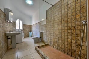 A bathroom with a sink, toilet, and shower area, featuring tiled walls and a tiled floor.