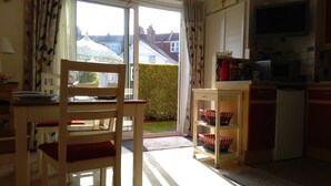 A kitchen with a dining area, a TV mounted above the counter, and a view of the outside through a sliding door. - Number Nine New Esplanade is a quiet coastal snug with a flat walk to the shore (Paignton)