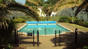 A swimming pool surrounded by palm trees and a fence. - Number Nine New Esplanade is a quiet coastal snug with a flat walk to the shore (Paignton)