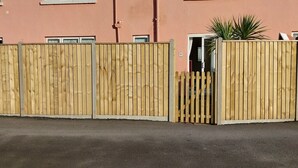 A wooden fence with a gate in front of a building with windows and a plant. - Number Nine New Esplanade is a quiet coastal snug with a flat walk to the shore (Paignton)