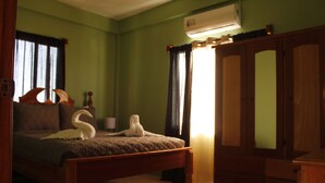 A bedroom with a bed, a wooden wardrobe, a window with curtains, and a wall-mounted air conditioner.