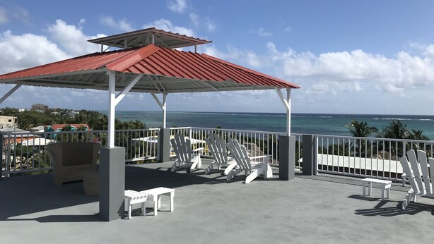 A covered outdoor seating area with a red roof, white railings, and a view of the ocean.