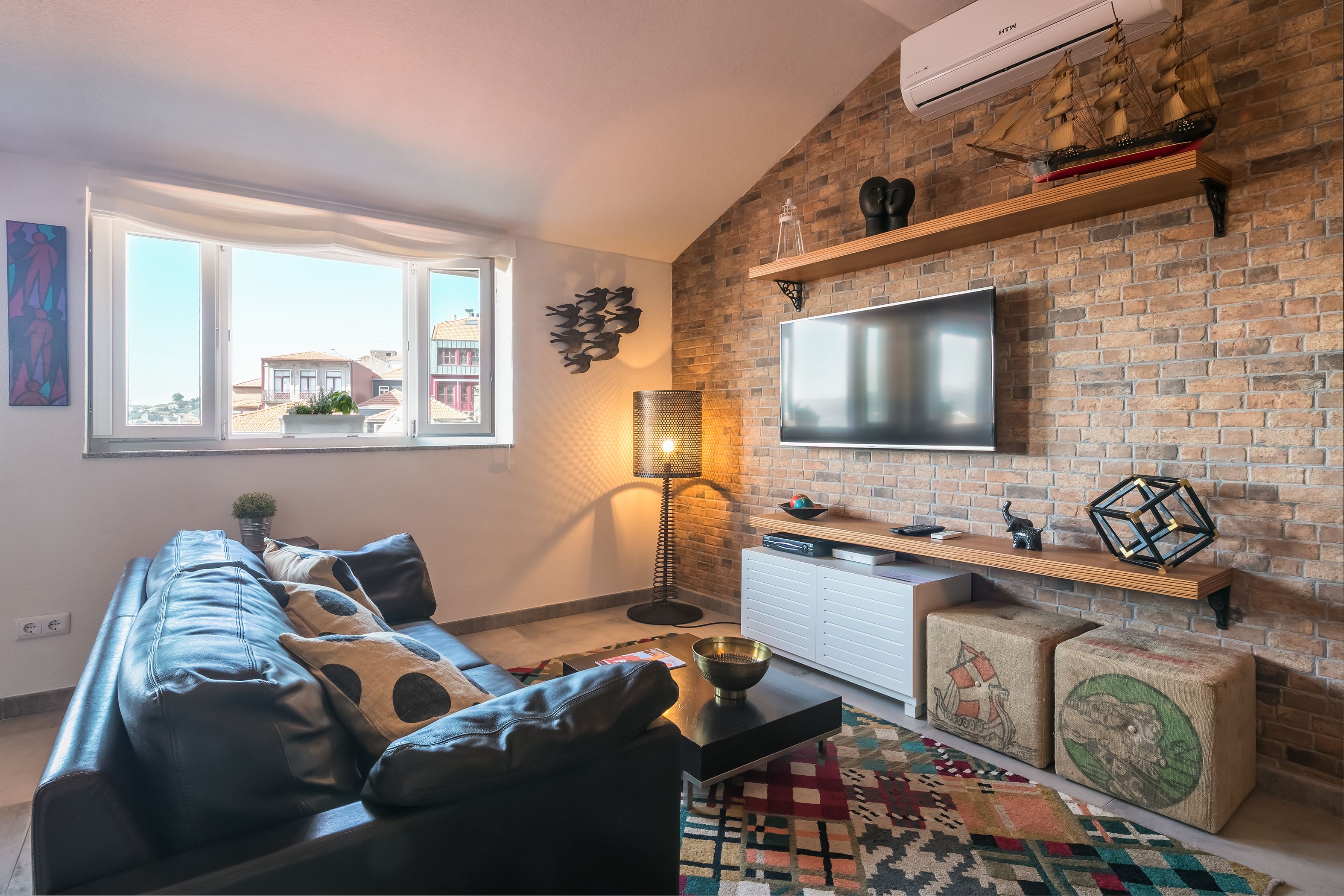 Un salon moderne avec un canapé en cuir, un téléviseur à écran plat, un mur en briques et une grande fenêtre.