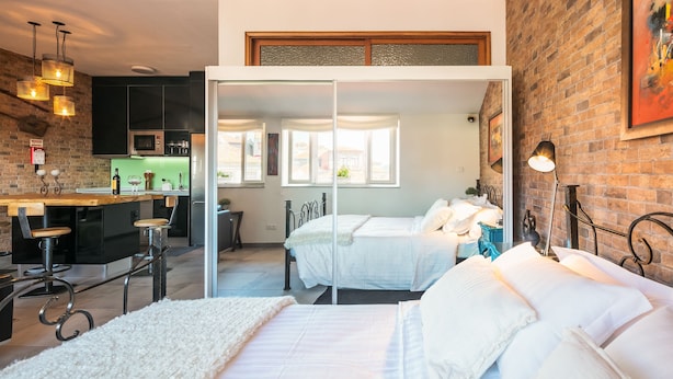 A modern bedroom with a large bed, a small desk, and a kitchen area visible through a glass door. - Merc Porto Ribeira's Up place (Porto)