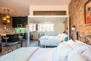 A modern bedroom with a large bed, a small desk, and a kitchen area visible through a glass door. - Merc Porto Ribeira's Up place (Porto)