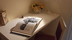A corner of a room with a white desk, a book, a small decorative item, and a vase with flowers. - APARTMENT CLOSE TO THE CATHEDRAL & RAILWAY STATION,WI-FI (Firenze)
