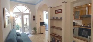 A living room with a sofa, a television, and a kitchen area with a refrigerator and stove.